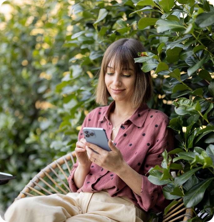 Frau sitzt im Grünen und schaut auf ein Smartphone