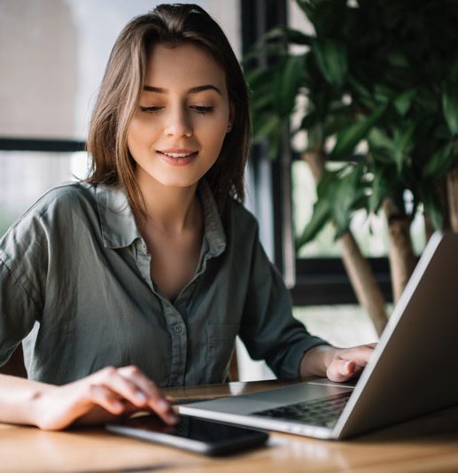 Frau arbeitet am Laptop an einem Schreibtisch mit Handy
