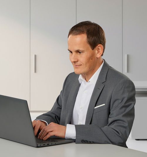 Herr Hölldobler im Business-Outfit sitzend am Laptop